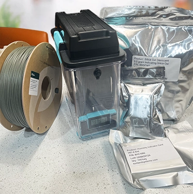 3d filament spool next to airtight container, humidity indicating cards, indicating silica desiccant packets, and dri-box