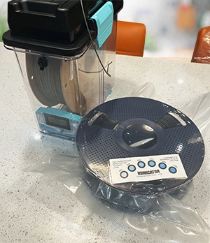 vacuum sealed roll of 3d printer filament next to sealed container for spool storage